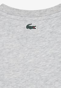 Ανοιχτό γκρι βαμβακερό t-shirt με στρογγυλή λαιμόκοψη, που διαθέτει ένα μικρό πράσινο λογότυπο κροκοδείλου και υφή με μελαν ζέ φινίρισμα.