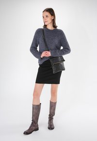 Grauer, flauschiger Pullover, schwarzer Rock und knielange braune Lederstiefel mit leichtem Glanz. Eine kleine schwarze Umhängetasche mit einem Reißverschluss-Detail.