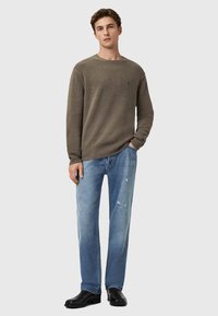 Olijfgroene gebreide trui met ronde hals, gedragen door een model in combinatie met lichtblauwe versleten jeans en zwarte schoenen. Casual pasvorm met geribbelde details.