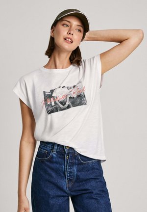 Vit kortärmad t-shirt med ett svartvitt fototryck och röd text. Matcher med högmidjade blå denimjeans. Justerbar keps.