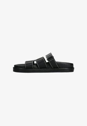 Sandales en cuir noir avec deux bandes horizontales, une ouverture pour le gros orteil et une semelle plate ; présente des coutures blanches contrastantes.