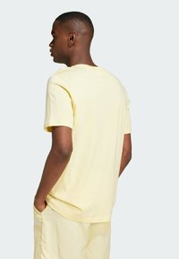 Camiseta de algodón amarilla clara de manga corta y escote redondo, mostrada por la parte de atrás con una textura suave y un diseño minimalista.