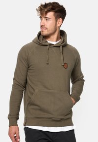 Sudadera verde oliva con una textura acogedora, mangas raglán, cordones ajustables y un bolsillo frontal. Presenta un pequeño parche de la marca.