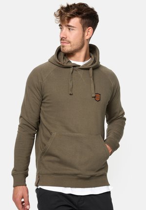 Sudadera verde oliva con una textura acogedora, mangas raglán, cordones ajustables y un bolsillo frontal. Presenta un pequeño parche de la marca.