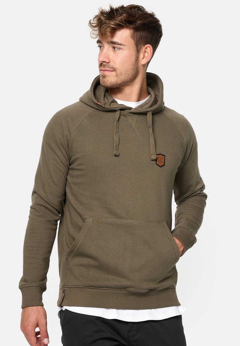 Sudadera verde oliva con una textura acogedora, mangas raglán, cordones ajustables y un bolsillo frontal. Presenta un pequeño parche de la marca.