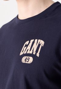T-shirt en coton bleu marine à col rond, avec un logo "GANT 49" imprimé en crème décoloré à l'avant. Texture douce.