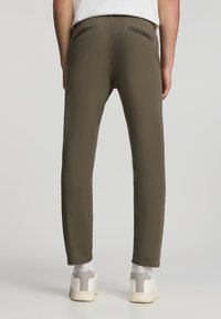 Pantaloni verde oliva dalla vestibilità slim, dotati di due tasche posteriori e una texture liscia, abbinati a sneakers bianche all'orlo.