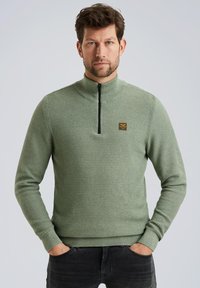 Groene gebreide sweatshirt met hoge kraag, halve rits aan de voorkant, geribbelde manchetten en een klein vierkant logo op de borst. G Combineert met donkere broek.
