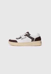 Hvit sneaker med brune semsket skinn- og lærdetaljer. Har en tykk kremfarget såle, rund tå og snøring. "justcavalli"-logoen er synlig.
