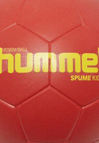 Roter Schaumstofffußball mit hexagonalem Muster und gelbem "hummel"-Logo. Die Oberfläche ist glatt mit leichtem Glanz und wurde für Kinder entworfen.
