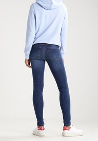 Sudadera azul claro, jeans ajustados azul oscuro y zapatillas blancas con acentos rojos. El conjunto presenta un diseño casual y una forma ajustada.