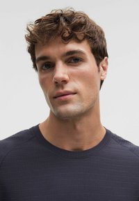 Granatowa koszula z krótkim rękawem wykonana z fakturowanej, prążkowanej tkaniny z okrągłym dekoltem. Zbliżenie na górną część ciała, podkreślające kołnierz i szwy na ramionach.