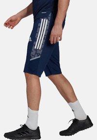 Marineblauwe sportshorts met witte verticale strepen en een gestructureerd zijpaneel. Gecombineerd met zwarte schoenen en witte sportsokken.