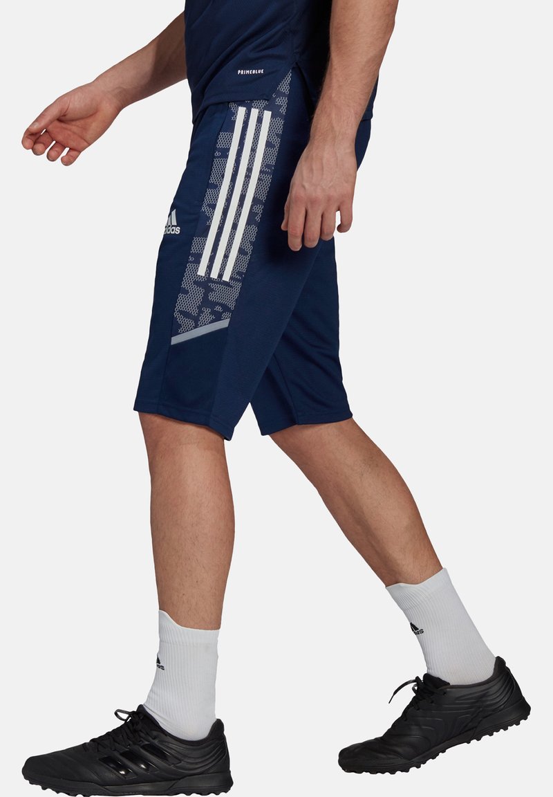 Marineblauwe sportshorts met witte verticale strepen en een gestructureerd zijpaneel. Gecombineerd met zwarte schoenen en witte sportsokken.