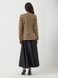 Veste marron ornée avec un motif floral, assortie à une jupe noire fluide. Elle possède des manches longues et une coupe ajustée. Escarpins noirs.