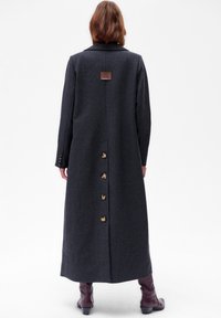 Lang, donkergrijze wollen jas met een gestructureerd ontwerp, met een achterventing en gouden knopen langs het midden. Bruin label op de kraag.