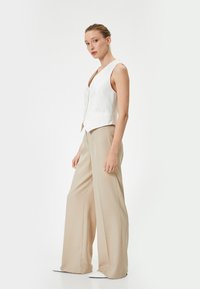 Witte linnen vest met een diepe V-hals en subtiele knopen, gecombineerd met losse beige broeken. Minimalistisch ontwerp, gladde textuur.