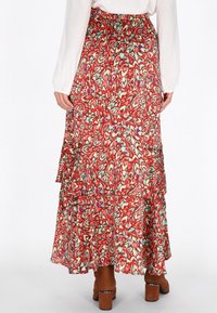 Fustă lungă cu un model floral vibrant în nuanțe de roșu, verde și alb, având volane stratificate. Asortată cu botine cu toc bloc maro.