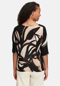Czarna i beżowa bluzka w wzory z rękawami o długości 3/4, z abstrakcyjnym wzorem i luźnym krojem. Miękka, lekka tkanina.