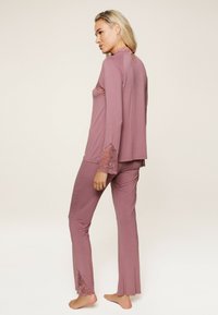 Ensemble de loungewear mauve avec des manches longues et des accents en dentelle. Le haut présente un dos en forme de trou de serrure ; le pantalon a des fentes sur les côtés et une coupe ajustée. Tissu doux.