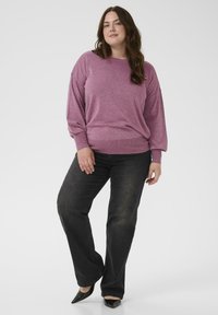 Lila strukturierter Pullover mit langen Ärmeln und geripptem Saum, kombiniert mit schwarzen geraden Jeans und schwarzen spitzen Schuhen.