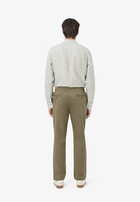 Gestreepte, knoop-up blouse in gedempt groen en wit; gecombineerd met olijfgroene broeken met een elastische tailleband en achterzakken.