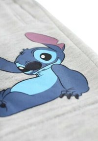 Tissu gris présentant un personnage de dessin animé bleu avec un accent rose. Le personnage a de grands yeux et est positionné allongé avec un bras tendu.