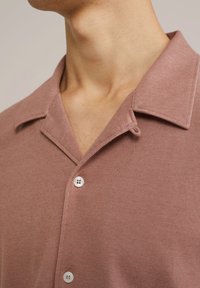 Camicia a maniche corte con colletto in tessuto rosa tenue a trama strutturata, caratterizzata da bottoni bianchi e un taglio morbido.