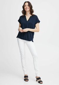 Top corto navy a maniche corte con scollatura a V, abbinato a pantaloni bianchi a taglio slim e sandali neri con tacco alto intrecciati. Un outfit semplice e casual.