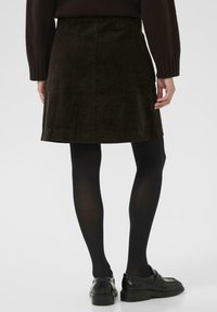 Jupe en velours côtelé marron au design droit, longueur au-dessus du genou, avec une texture subtile, assortie à des collants noirs et des chaussures.
