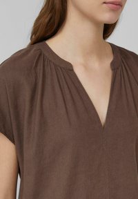 Haut en lin marron avec un design à col en V. Texture douce avec des fronces aux épaules et un détail de couture net et simple le long du devant.