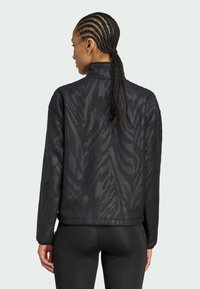 Veste zippée noire avec un motif zèbre texturé, col montant et coupe décontractée. Le matériau semble doux avec un léger éclat.