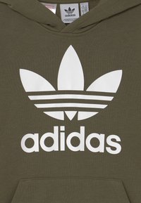 Olivgrön hoodies med en stor vit Adidas trefoil-logotyp och text. Tillverkad av mjukt tyg med en känguruficka och huva.