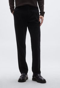 Juodos tiesaus kirpimo kelnės su šoninėmis kišenėmis, pagamintos iš lygios medžiagos. Priderintos prie elegantiškų juodų batų, minimalistinio dizaino.