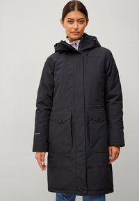 Zwarte parka met een capuchon, voorzien van een rits- en knoopsluiting, twee voorzakken en een zachte textuur. Lange mouwen met gestikte details.