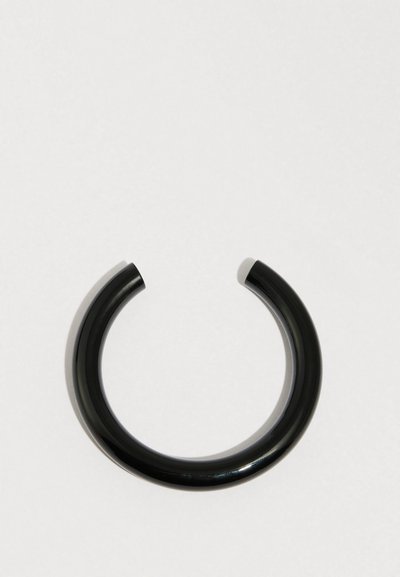 Musta, pyöreä rannekoru, joka on valmistettu sileästä, kiiltävästä materiaalista. Siinä on paksu, minimalistinen muotoilu saumattomalla, avoimella päällä.