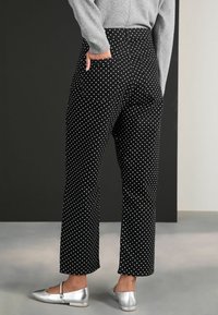 Pantaloni negri cu buline albe, cu design drept, talie înaltă și buzunare la spate. Asortați cu pantofi plata metalici argintii.