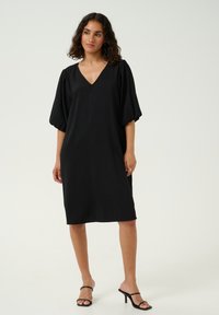 Black dress with a V-neck, short puff sleeves, and a loose fit. Made from textured fabric, knee-length with a simple, modern design.