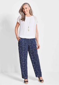 Weißes kurzärmliges Oberteil kombiniert mit navyblauen gemusterten weit geschnittenen Hosen mit weißen Punkten, ergänzt durch eine lange Halskette und Espadrilles.