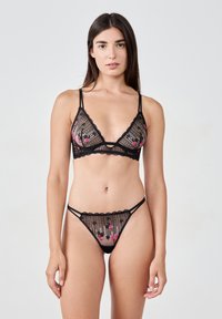 Ensemble de lingerie en dentelle noire comprenant un bralette triangle et un string avec broderies florales, panneaux transparents et bords festonnés.