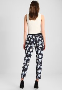 Květinové kalhoty z černé látky s jemnými modrými magnoliemi. Navrženy v úzkém střihu, s černým pasem a délkou ke kotníkům.