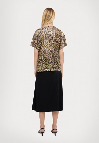 Maglietta a maniche corte con fantasia leopardata, decorata con paillettes dorate e marroni, abbinata a una gonna nera fino al ginocchio e tacchi neri.