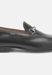 Mocassins en cuir noir avec un bout arrondi, accents en métal décoratifs, couture discrète et design allongé. Talon plat et finition lisse.