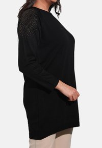 Black long-sleeve tunic made of soft fabric, featuring rhinestone embellishments on the shoulders, with a relaxed fit and ribbed cuffs.