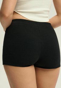 Czarne szorty ribbed o dopasowanym kroju, z bezszwowym pasem i minimalnym przeszyciem wzdłuż krawędzi dla gładkiego wyglądu.