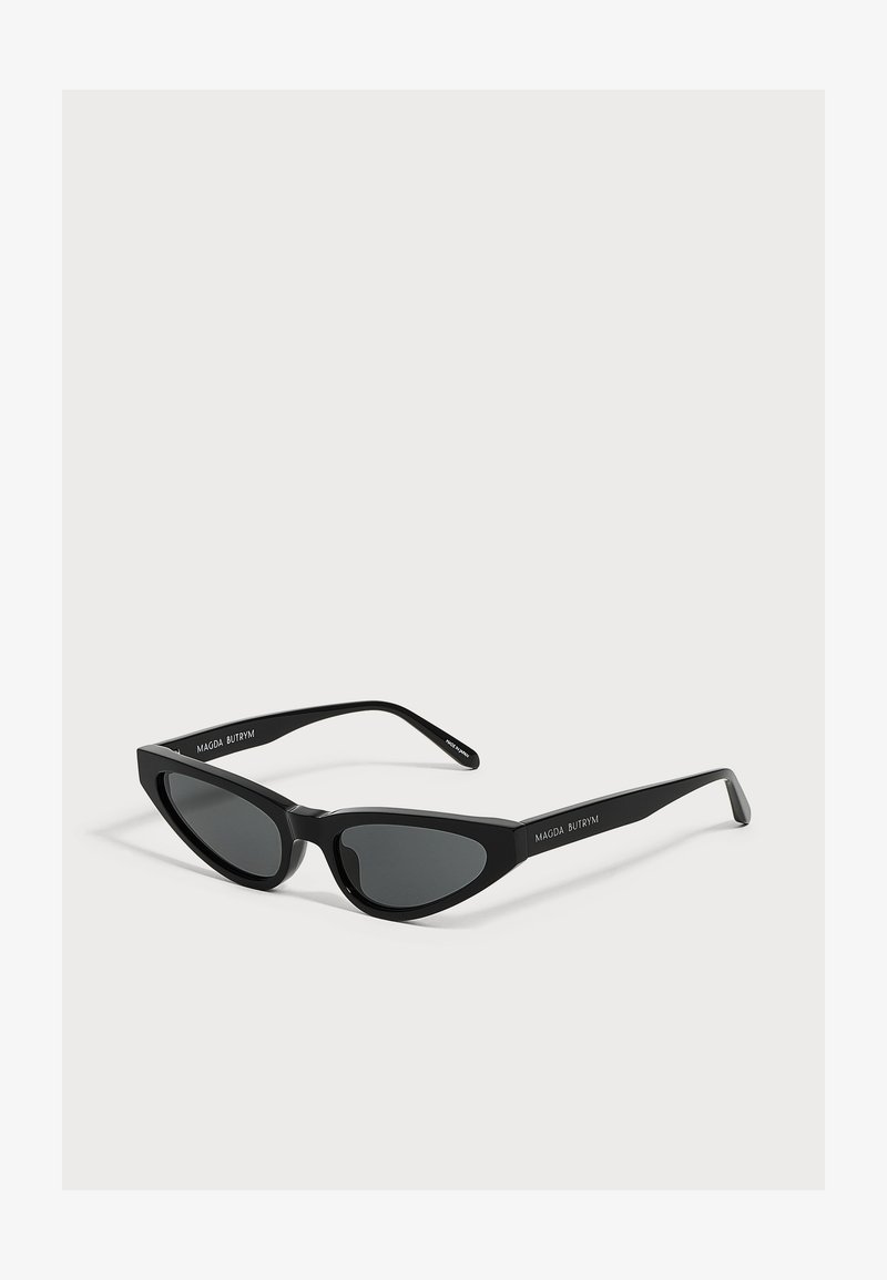 Lunettes de soleil noires forme œil de chat avec verres foncés et branches fines, marquées "MAGDA BUTRYM" sur le côté.