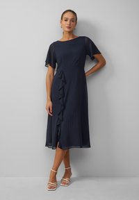 Navy blauwe jurk van lichte stof, met korte vleugelmouwen en een ruchesdetail aan de voorkant, tot net onder de knie.