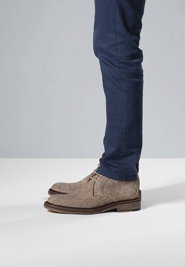 Brown felt ankle boots with a rounded toe, leather accents, and a rubber sole, paired with dark blue fitted trousers.