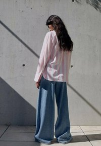 Langarmshirt in hellrosa und weißen Streifen, kombiniert mit weit geschnittenen Jeans in Blau. Glatte Stoffoberfläche, lässiger Schnitt, minimalistisches Design.