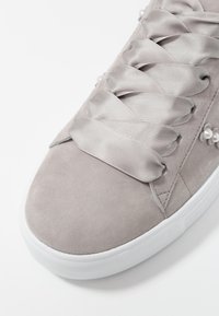 Sneaker in suede grigio chiaro con larghe lace in satin e piccole perle decorative sui lati, suola in gomma bianca.